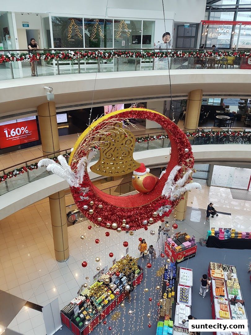 A festive Christmas decoration hangs in a shopping mall atrium with shops and people below.