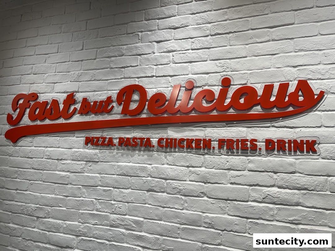 A red sign on a white brick wall reads 'Fast but Delicious' and lists menu items.