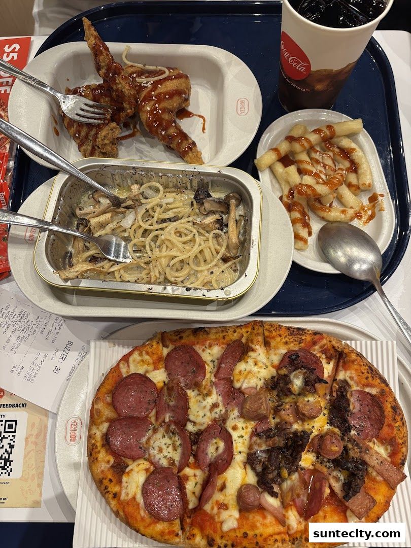 A tray of food including pizza, fried chicken wings, pasta, fries, and a drink.