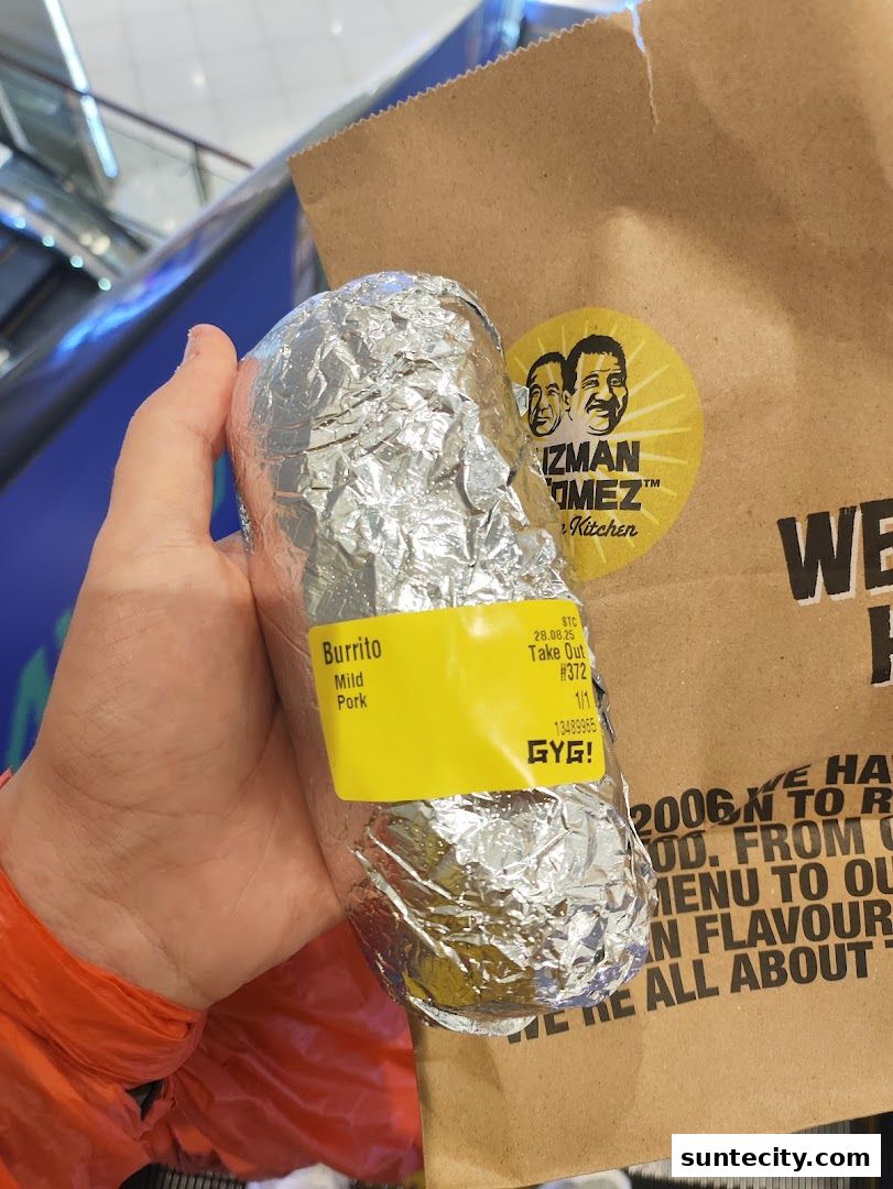 A hand holds a foil-wrapped burrito with a Guzman y Gomez bag in the background.