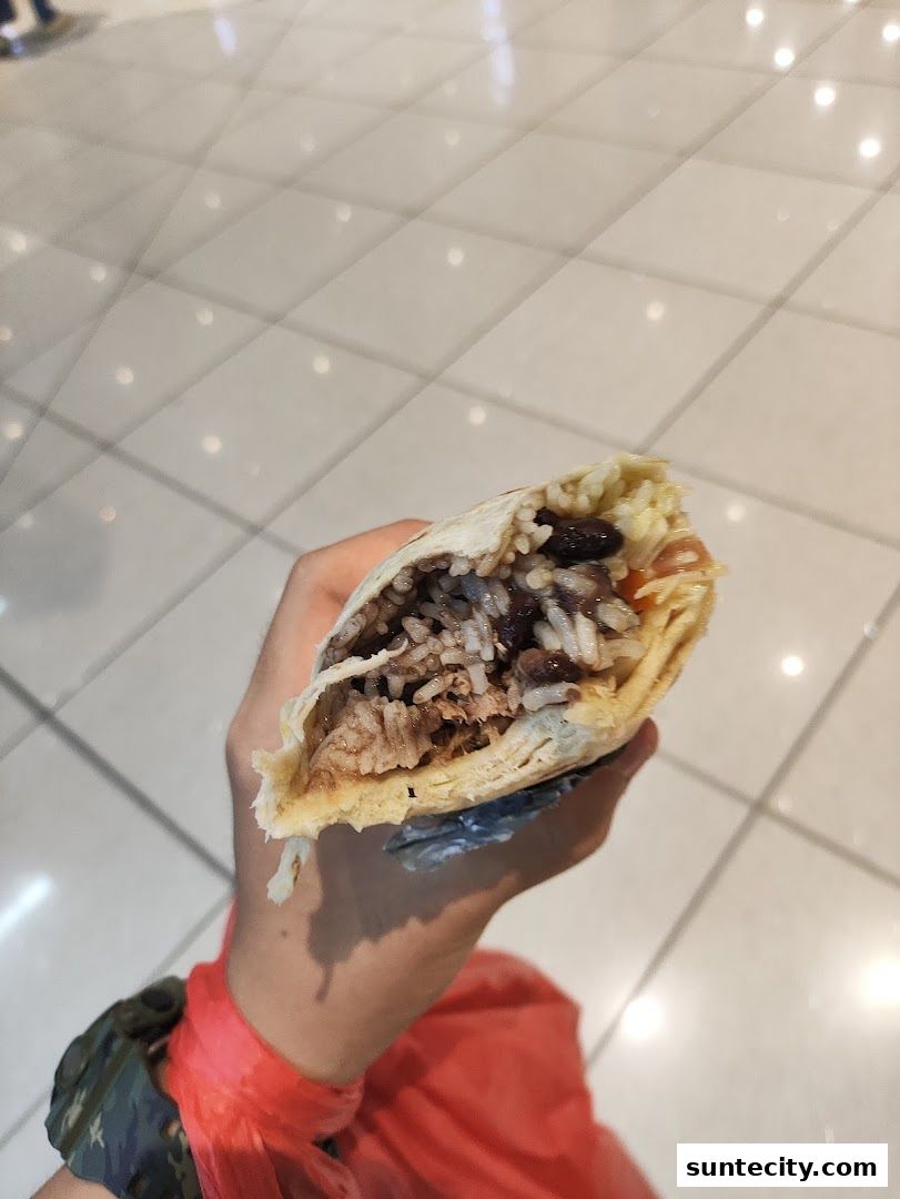 A hand holds a partially eaten burrito filled with rice, beans, and meat.