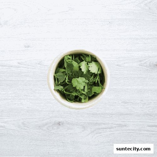 A bowl of fresh, chopped cilantro on a white wooden surface.