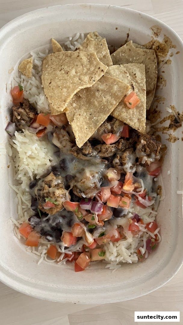 A close-up of a delicious burrito bowl with rice, beans, meat, salsa, and tortilla chips.