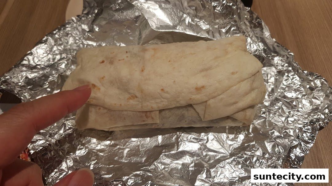 A hand points to a freshly wrapped burrito on a bed of crinkled aluminum foil.