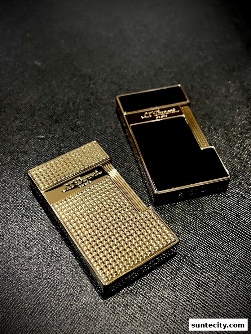Two elegant S.T. Dupont lighters, one gold and one black, displayed on a textured surface.