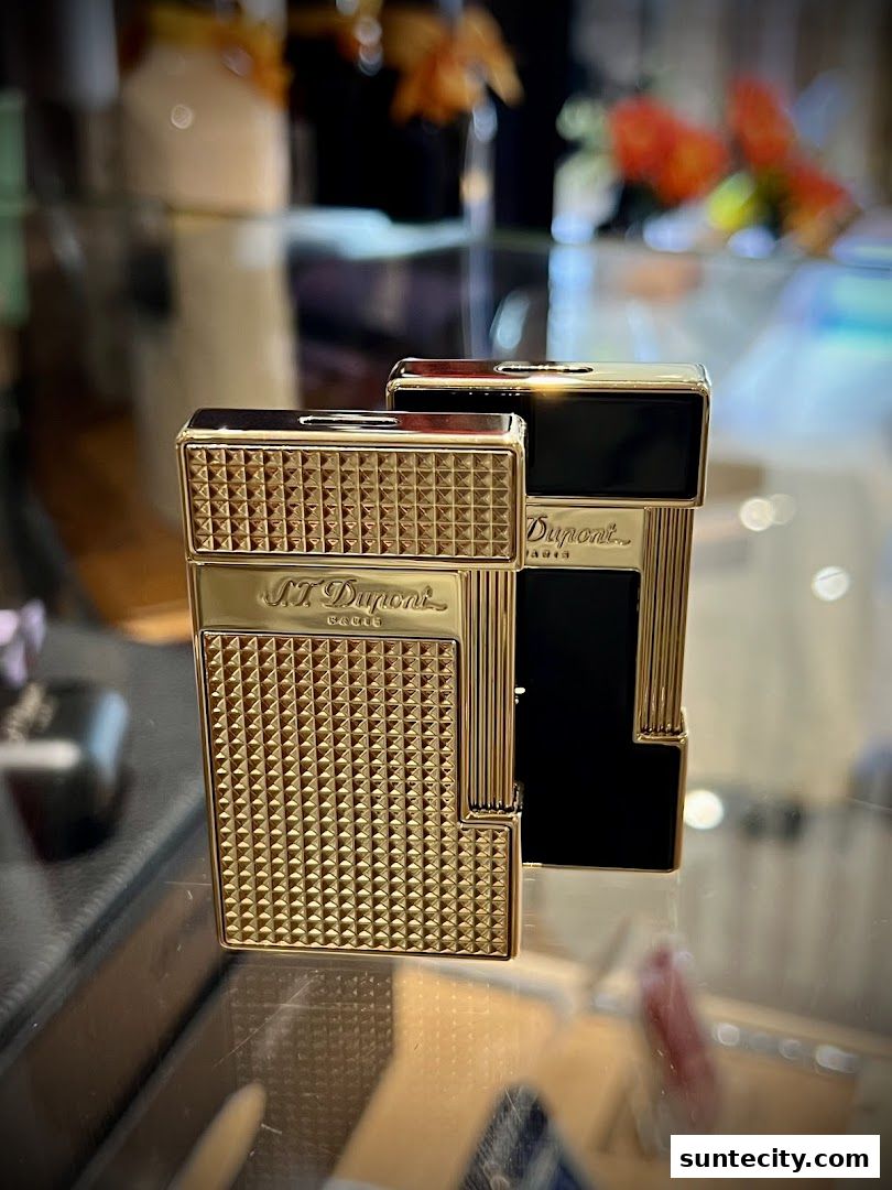 Two elegant S.T. Dupont lighters, one gold and one black, displayed on a reflective surface.