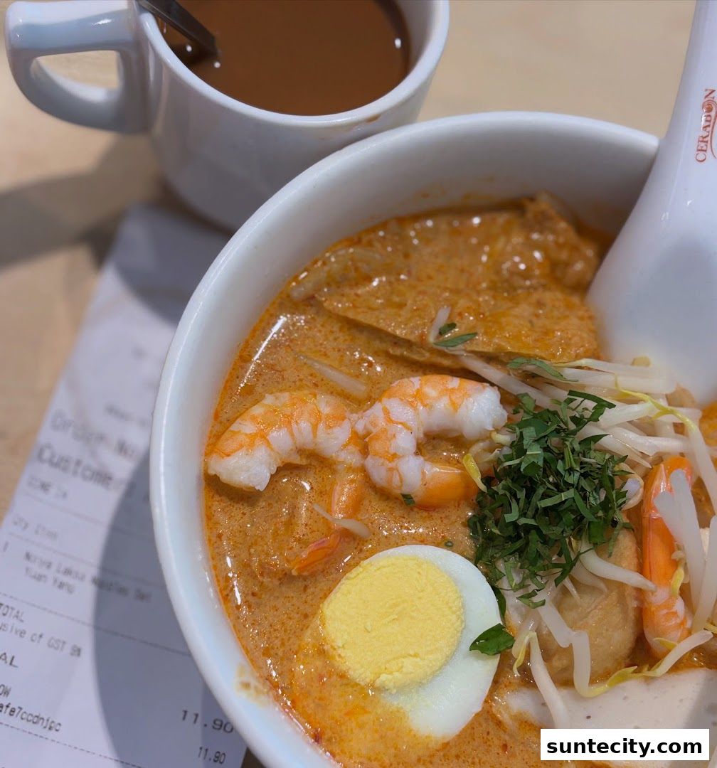 A close-up of a bowl of Laksa with prawns, egg, and bean sprouts, next to a cup of coffee.