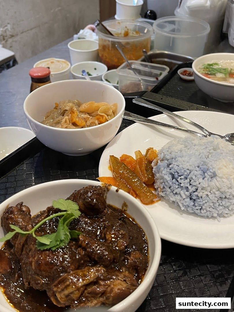 A close-up of a delicious Peranakan meal with braised chicken, blue pea rice, and side dishes.