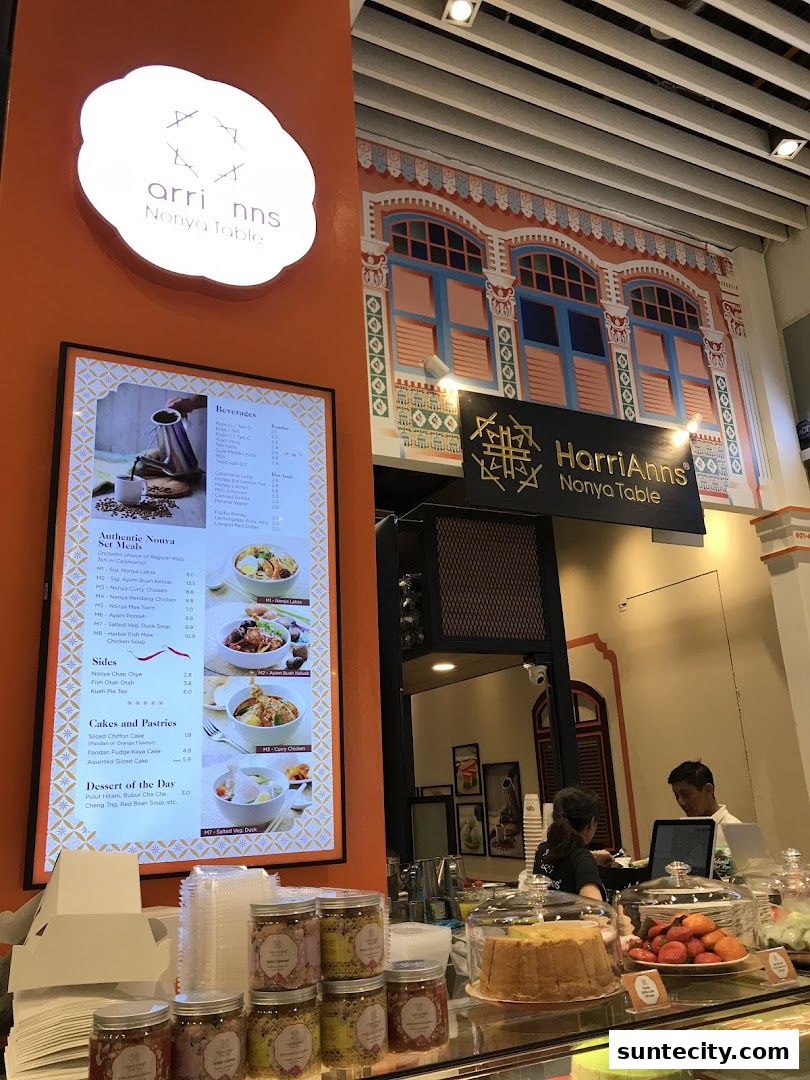 A brightly lit shop interior with a menu board, display of cakes, and staff serving customers.