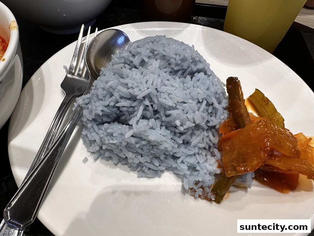 A plate of blue-tinged rice served with a side of savory stewed vegetables.