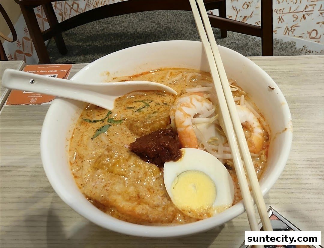 A bowl of delicious Laksa with shrimp, egg, and chili paste, served with chopsticks and a spoon.
