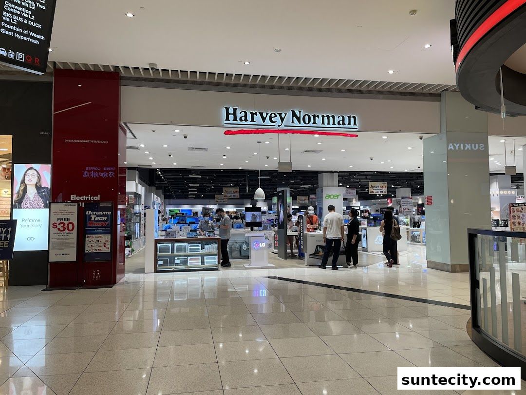 The entrance of Harvey Norman Suntec City, showcasing electronics and appliances with shoppers inside.