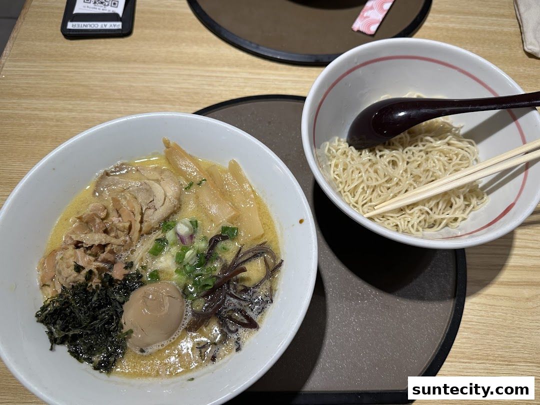 A bowl of ramen with chicken, egg, and bamboo shoots, served with a side of noodles.