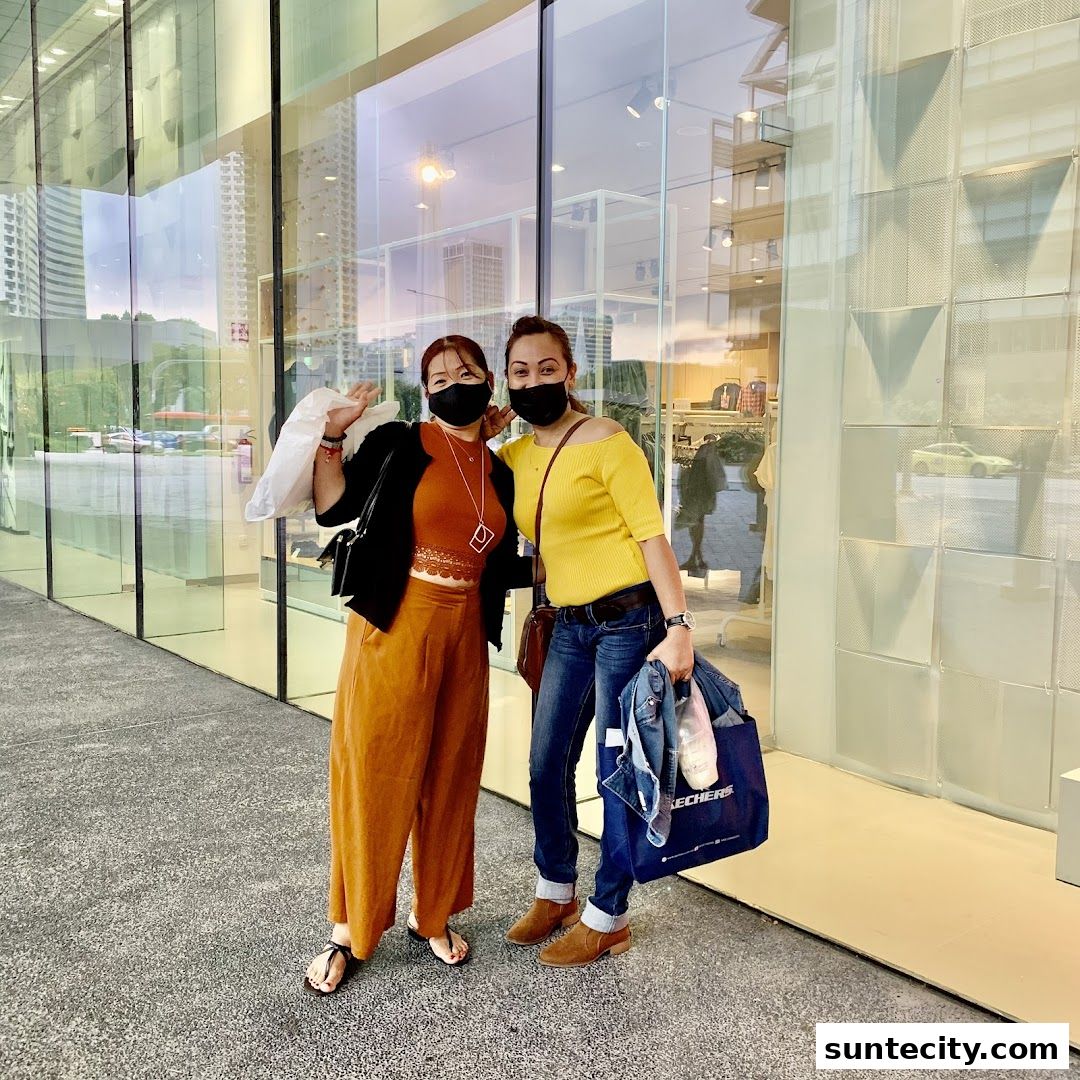 Two women posing in front of a store with large glass windows, holding shopping bags.