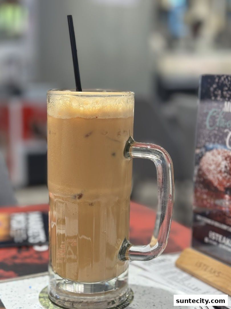 A tall glass of iced coffee with a straw sits on a table at iSTEAKS.