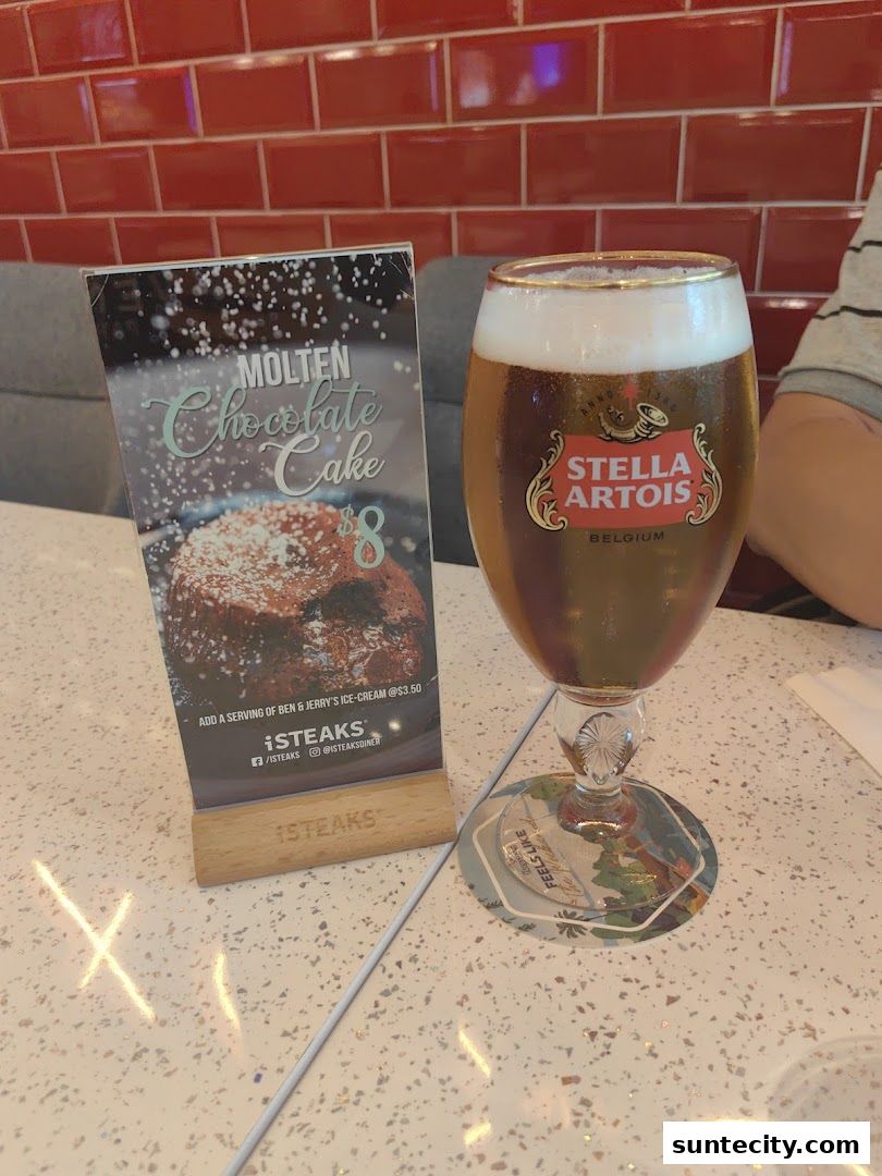 A table at iSTEAKS with a menu featuring Molten Chocolate Cake and a glass of Stella Artois beer.