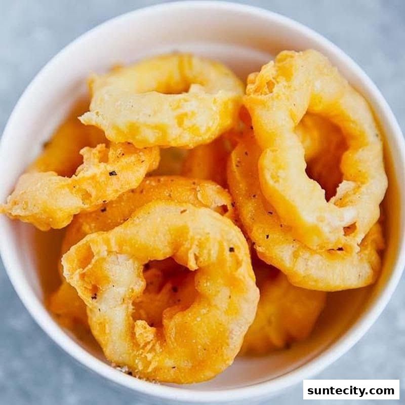 A close-up shot of crispy, golden-brown onion rings in a white bowl.