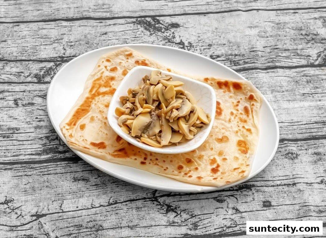 A plate of prata with a side of sliced mushrooms on a wooden table.