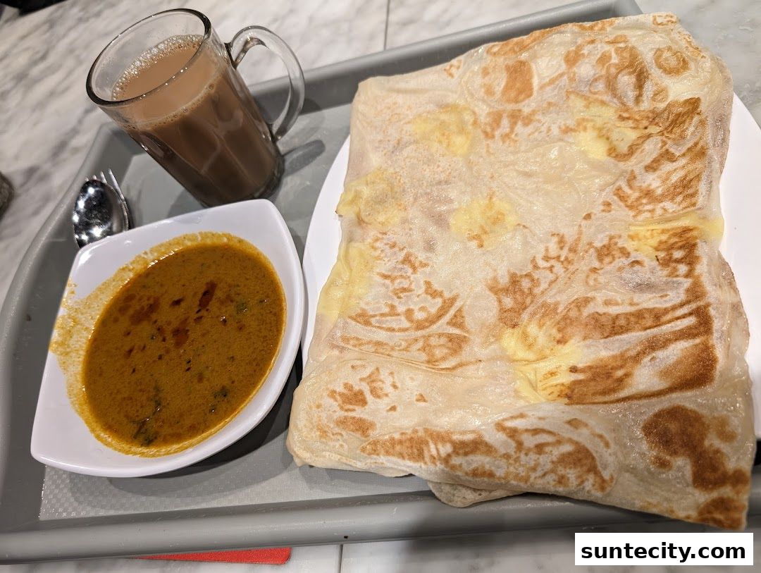 A close-up of a prata with curry and a cup of teh tarik on a tray.