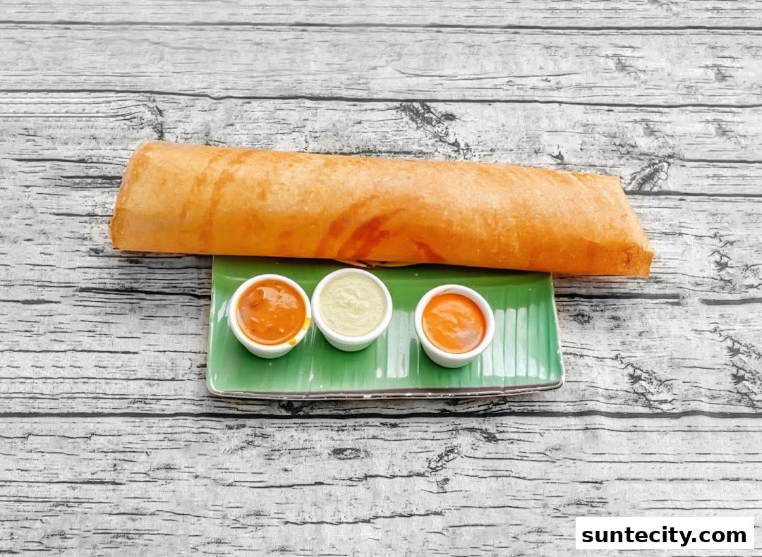 A long, golden-brown dosa served with three small bowls of dipping sauces on a green plate.
