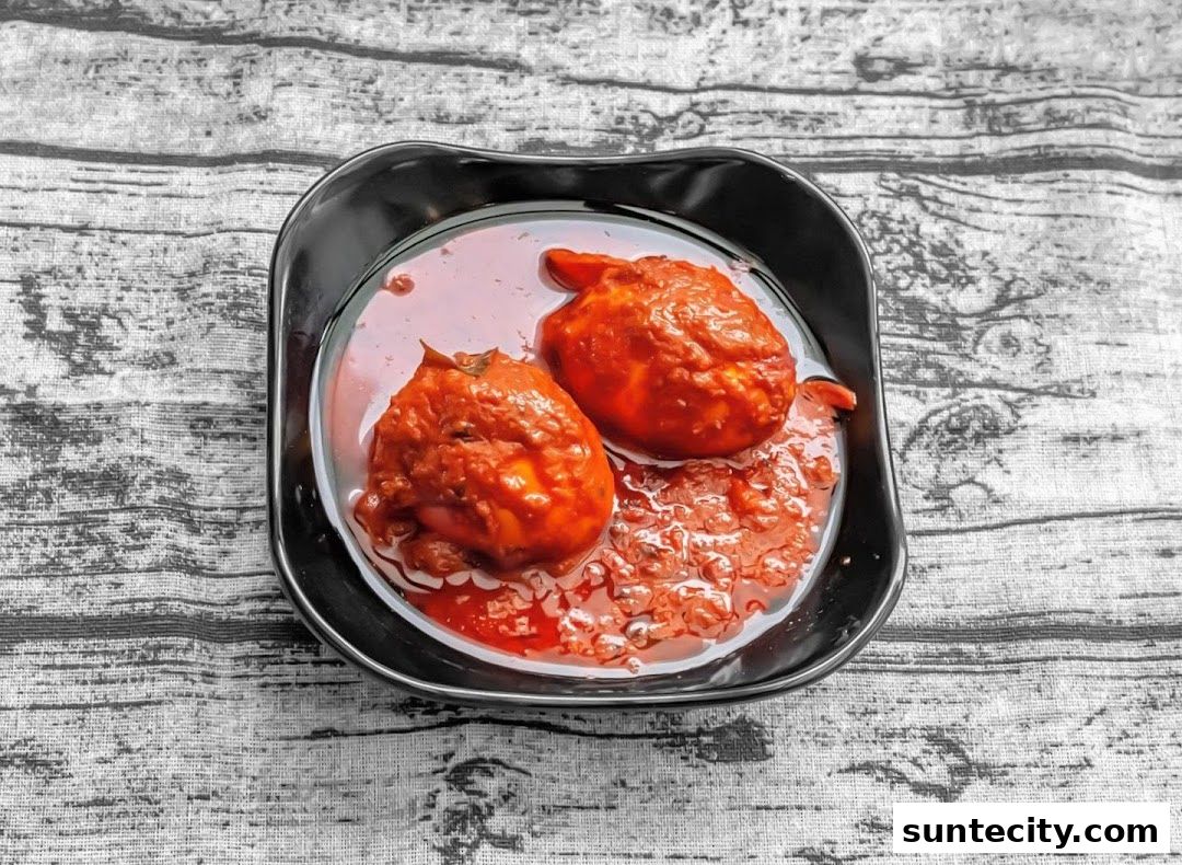 Two hard-boiled eggs in a rich, red curry sauce served in a black bowl.