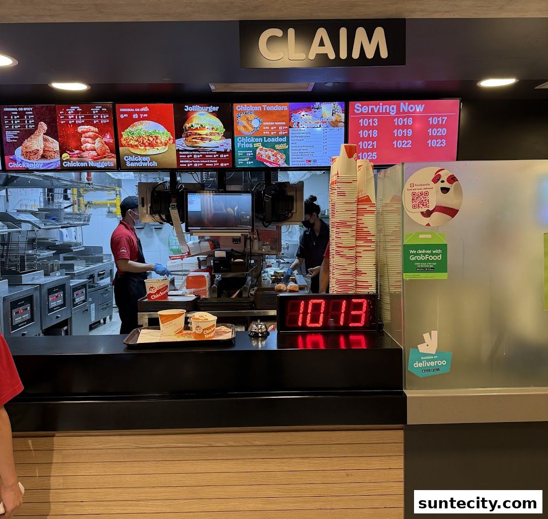 Jollibee counter with staff preparing food and digital menu boards displaying food items.
