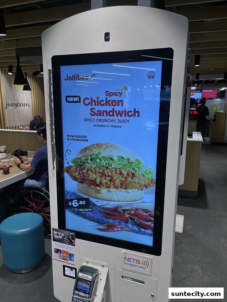 A Jollibee self-order kiosk displays a new Spicy Chicken Sandwich with price and details.
