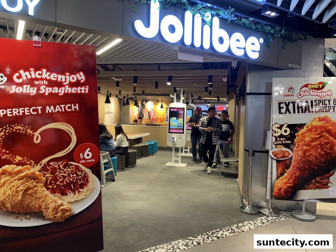 The entrance of a Jollibee restaurant with promotional posters and customers inside.