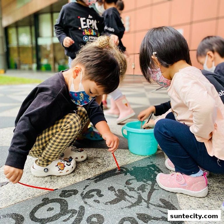 Children wearing masks engage in an outdoor art activity, painting on the ground.