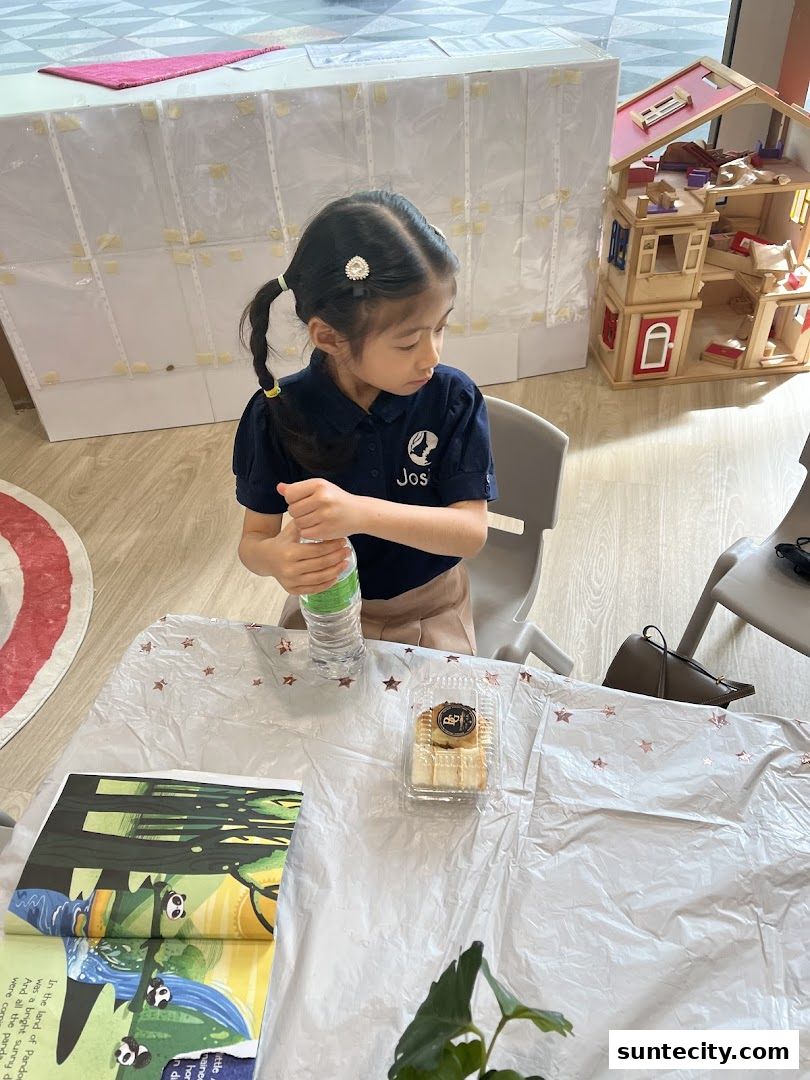 A young girl in a school uniform sits at a table with a book and a snack.