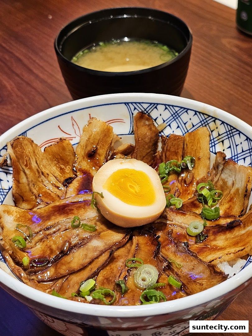 A close-up of a delicious Japanese rice bowl topped with grilled pork and a soft-boiled egg.