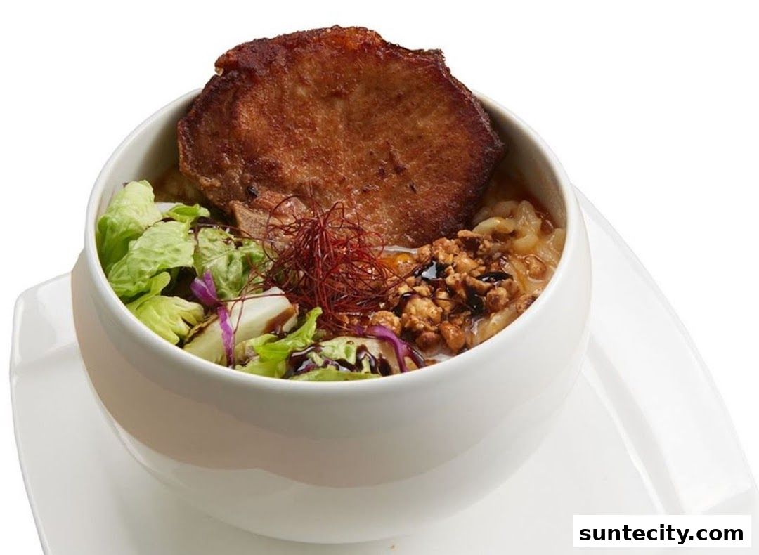 A bowl of ramen with a thick slice of pork and fresh vegetables.