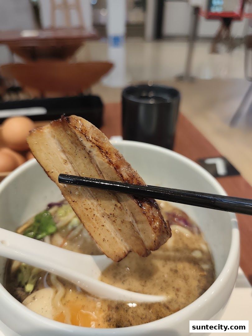 A close-up shot of a piece of chashu pork being lifted from a bowl of ramen.