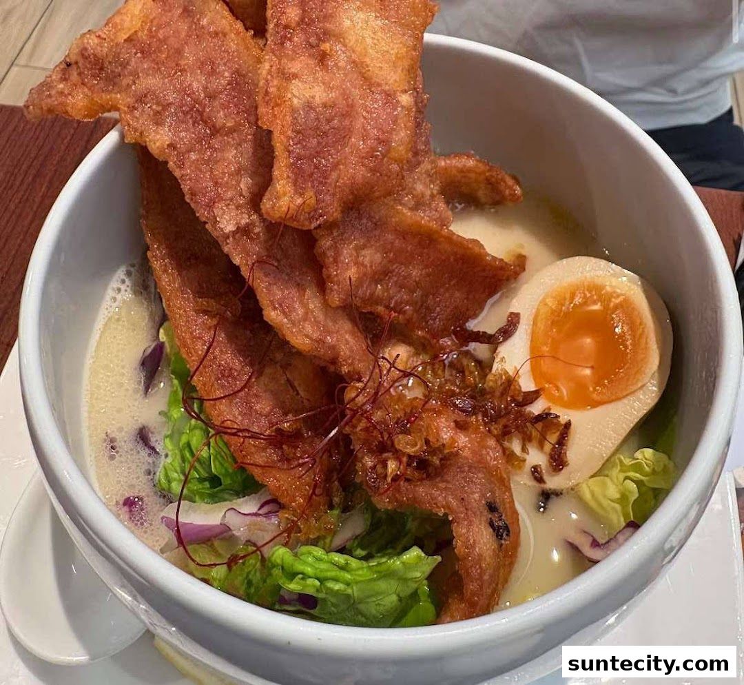 A close-up of a bowl of ramen with crispy pork belly, a soft-boiled egg, and fresh vegetables.