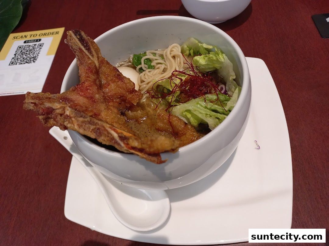 A bowl of ramen with a large piece of fried fish and vegetables.
