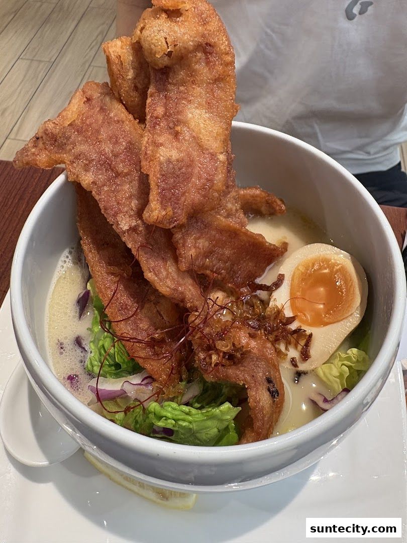 A bowl of ramen with crispy pork belly, a soft-boiled egg, and fresh vegetables.