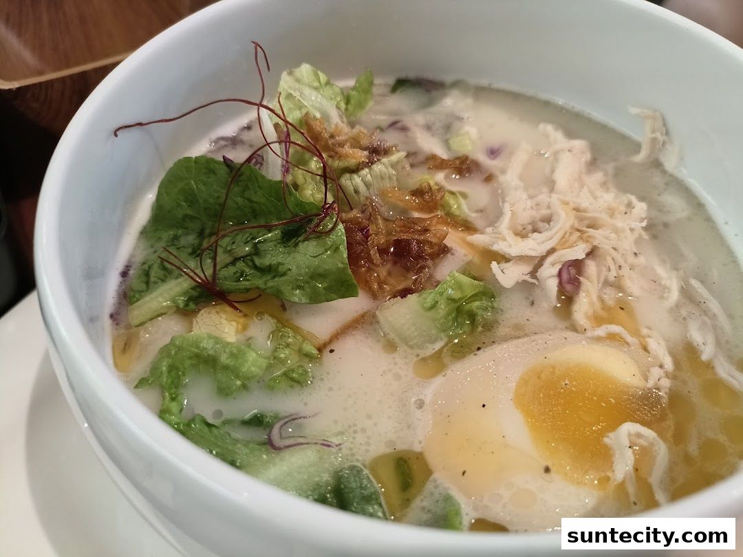 A close-up of a bowl of ramen with shredded chicken, a soft-boiled egg, and fresh vegetables.