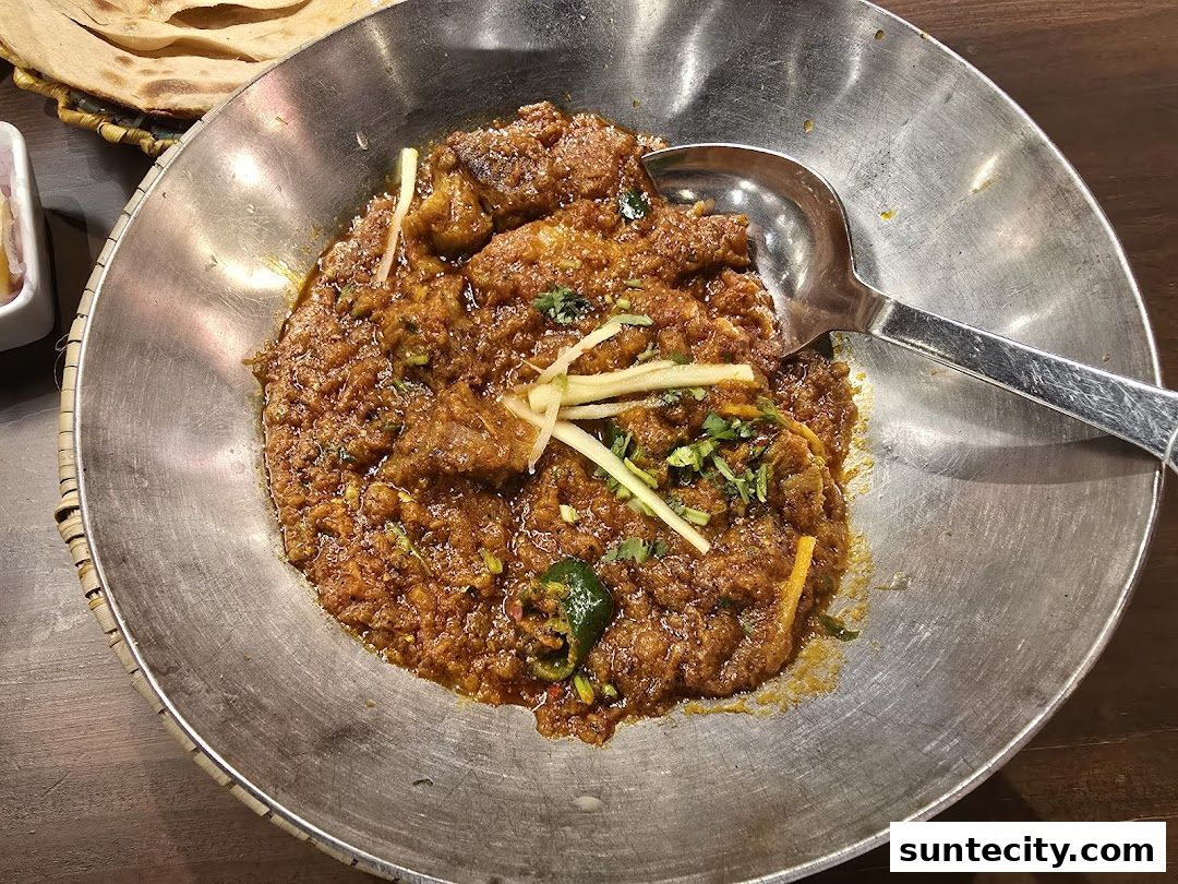 A close-up shot of a flavorful meat dish served in a metal bowl with naan bread.