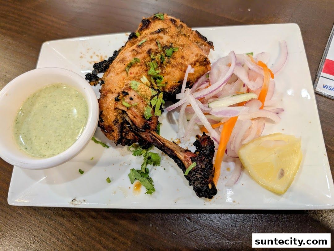 A plate of grilled lamb chops with a side of mint sauce, salad, and lemon.