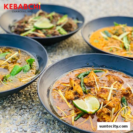 Four bowls of delicious, savory dishes from Kebabchi Charcoal BBQ, garnished with lime and herbs.