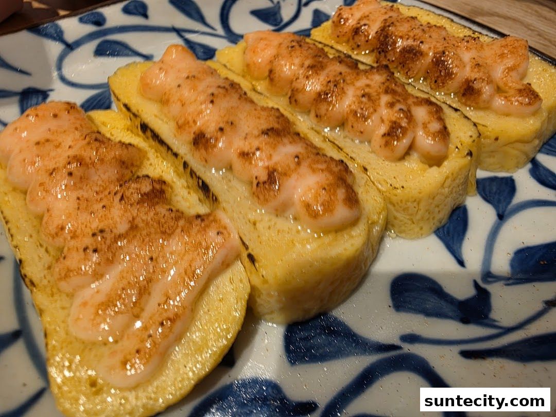 Close-up of tamagoyaki topped with torched salmon and sprinkled with spices.