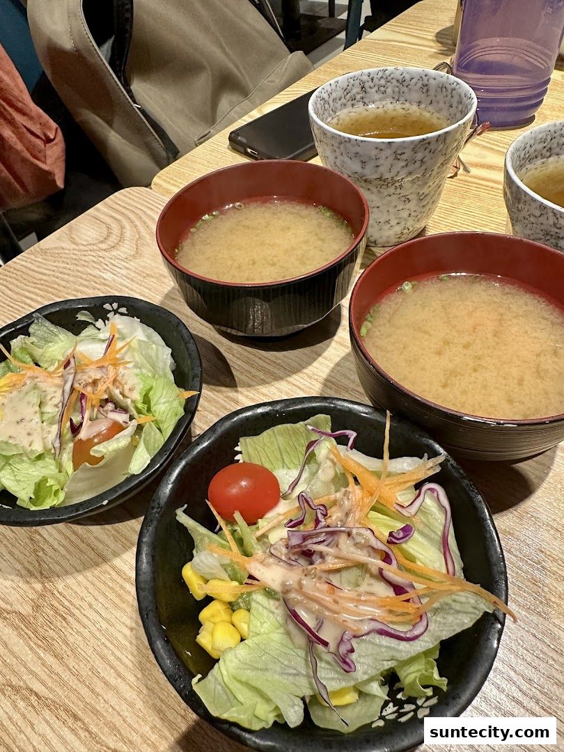 Two salads and two bowls of miso soup are served on a wooden table.