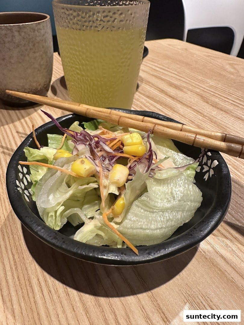 A fresh salad with corn and shredded vegetables served with chopsticks and a drink.