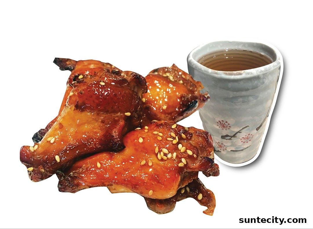 A close-up of glazed chicken wings sprinkled with sesame seeds next to a cup of tea.