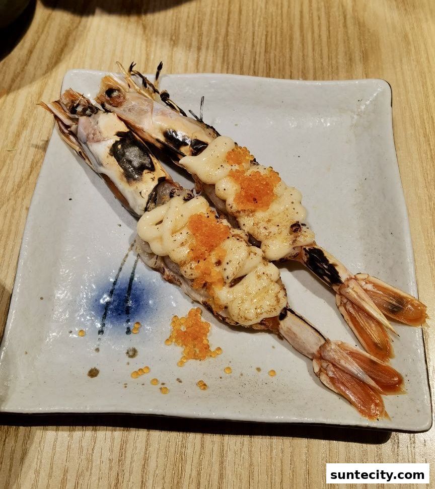 Two grilled prawns topped with creamy sauce and roe on a square plate.