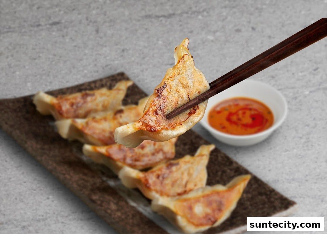 Chopsticks lifting a golden-brown gyoza from a plate with dipping sauce.