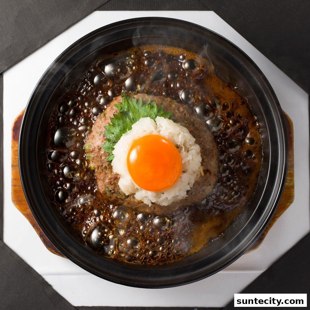 A close-up overhead view of a steaming hamburger steak topped with grated daikon and a raw egg yolk.