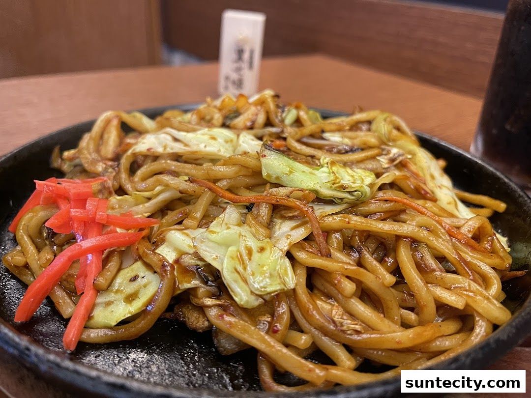 A close-up shot of a steaming plate of yakisoba noodles with cabbage and pickled ginger.