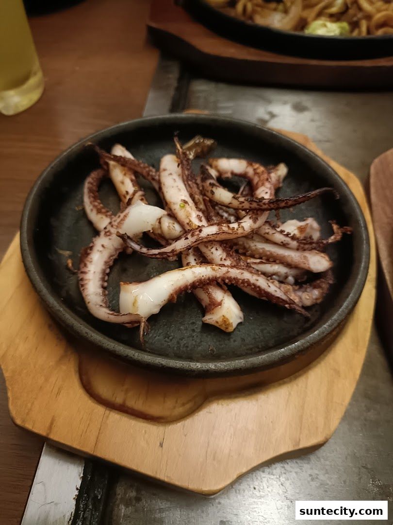 A close-up shot of grilled squid tentacles served on a black plate with a wooden base.