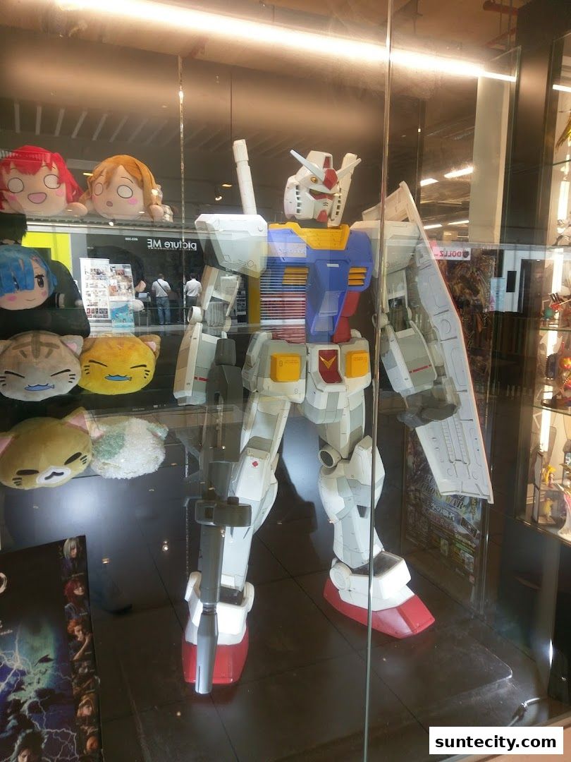 A large Gundam statue is displayed in a shop window with plush toys.